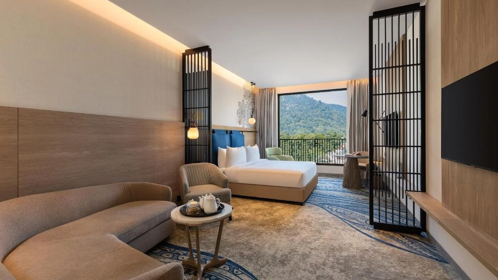 Spacious modern hotel suite with curved sofa lounge, king bed, and scenic mountain view window.