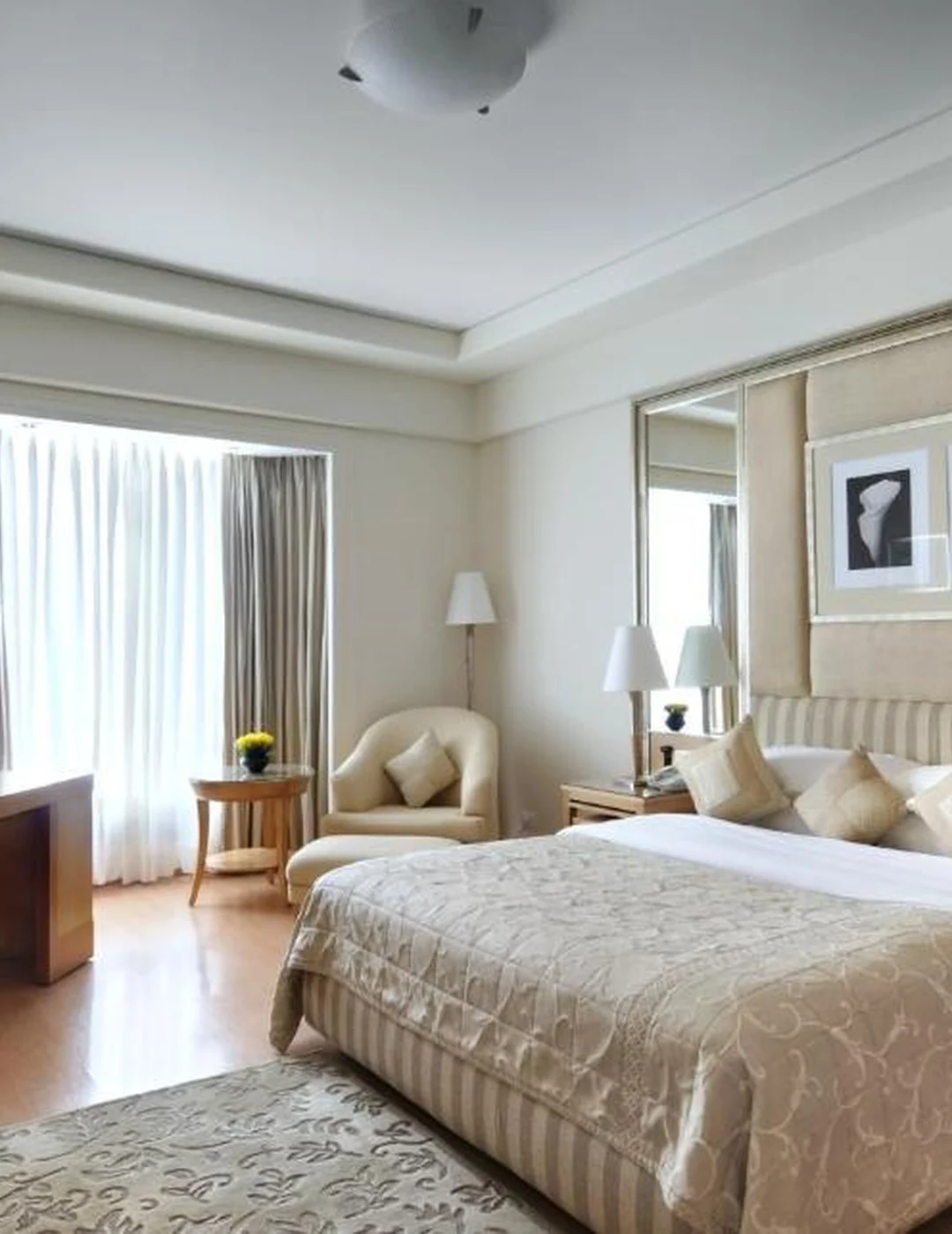 Luxury hotel room suite interior with king bed, plush bedding, and large window.