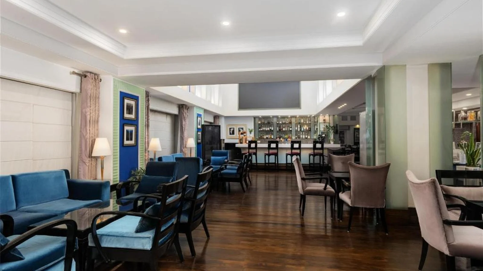 Hotel lounge and bar interior with blue plush armchairs, wooden flooring, and counter seating.