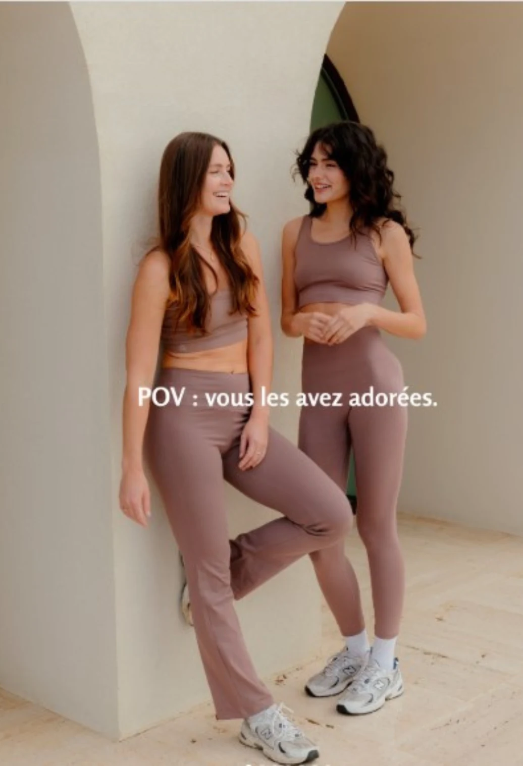 Two women wearing matching mauve activewear sets standing near an archway.