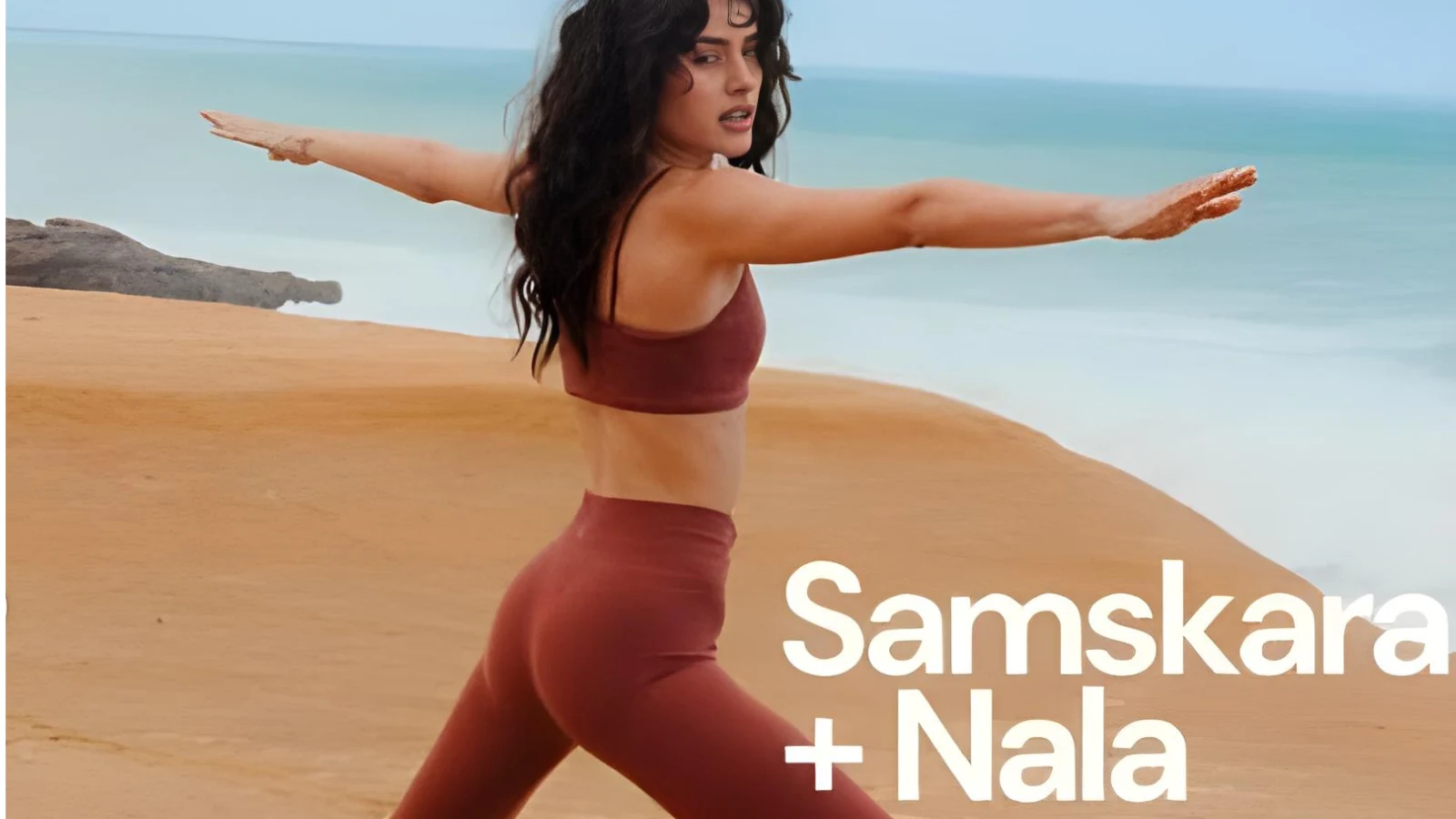 Woman practicing yoga Warrior pose on the beach in mauve activewear labeled Samskara + Nala.
