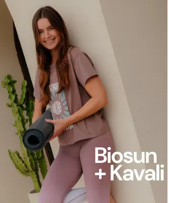 Woman holding a rolled yoga mat in mauve lounge set labeled Biosun + Kavali.