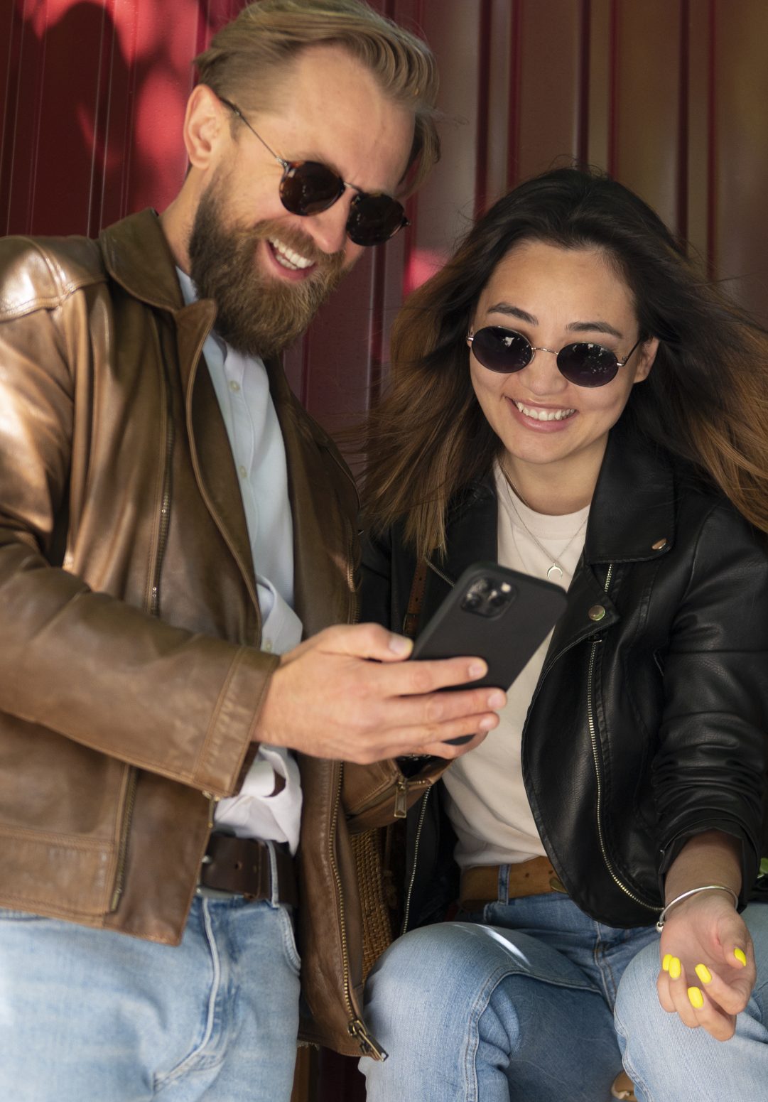 couple-wearing-synthetic-leather-jackets-using-smartphone-outdoors